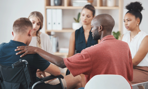 five people sit around in a circle in a group session learning about virtue recovery houston and its treatment programs as one member consoles another member