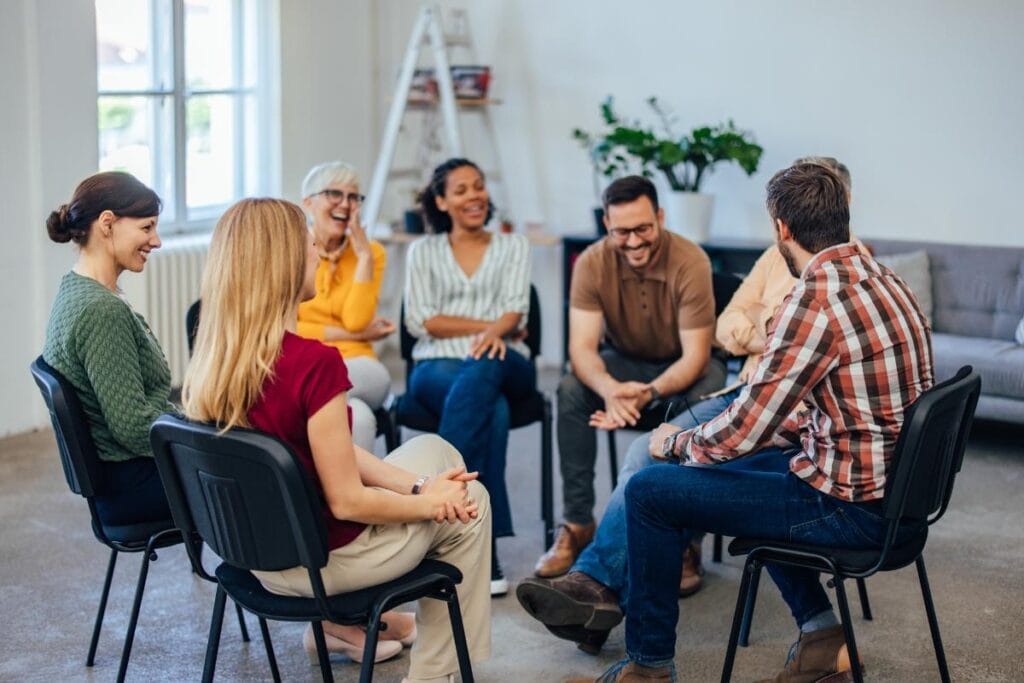 people in a group therapy session sit together in a circle and are laughing