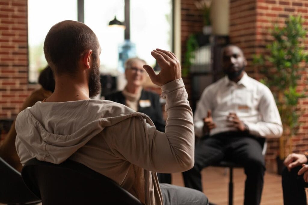 man raises his hand in group therapy session