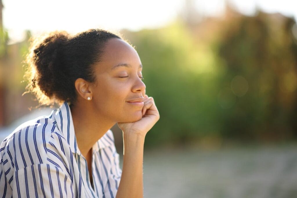 woman sits outside with her eyes closed and smiles