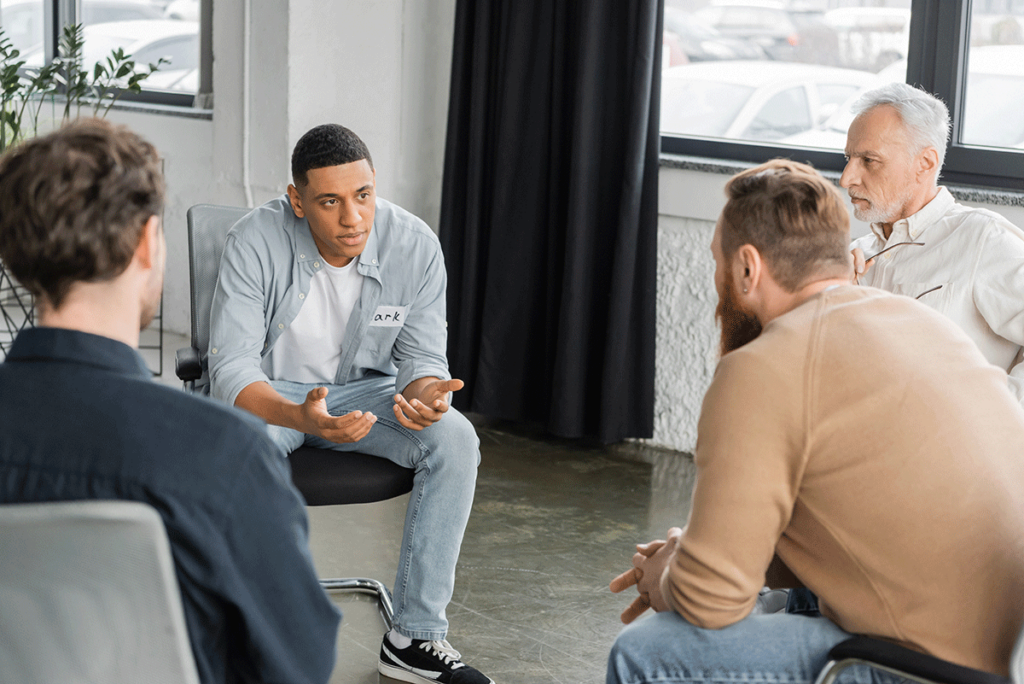 a man sits and talks to group members in a session at the mans men's rehab program in houston tx