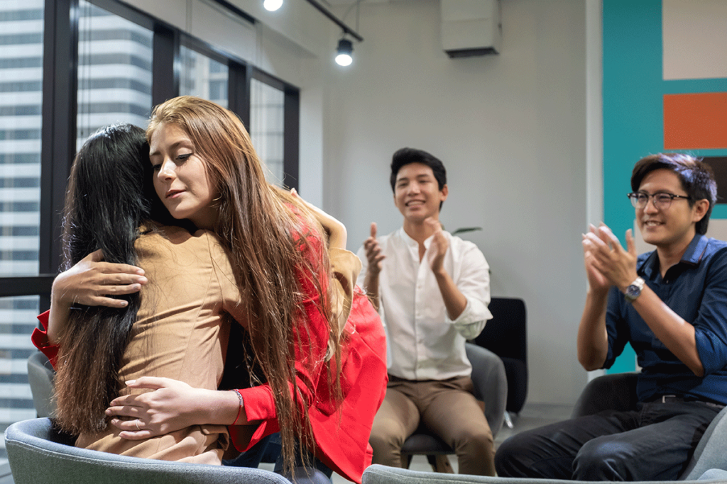 a group member hugs another group member while other members clap support is one of the biggest group therapy advantages